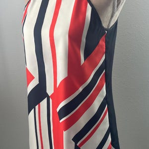 May include: Sleeveless top with a striking geometric pattern. The design features bold vertical and diagonal stripes in red, white, and navy blue. The top has a halter neckline and a solid black back panel.