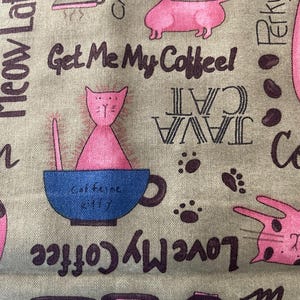 May include: A fabric with a repeating pattern of pink cats, coffee cups, and coffee beans on a tan background. Text includes "Get Me My Coffee", "Java Cat", and "Meow Latte". The design has a whimsical, playful theme.