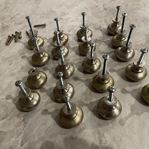 May include: A collection of antique-style cabinet knobs with a brass finish. Each knob has a rounded shape and is attached to a long screw. Several additional screws are also present, suggesting a hardware set for furniture restoration or new construction.