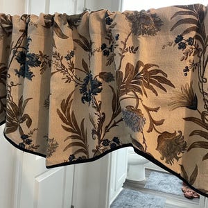 May include: A valance curtain with a beige background and a floral pattern in shades of brown and blue. The curtain has a black border and is hanging above a white door.