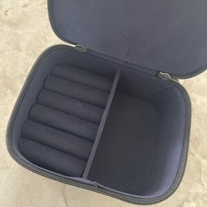 Op de afbeelding: Open marineblauwe sieradendoos met ritssluiting. De binnenkant heeft ringsleuven en een verdeeld compartiment. De doos is gevoerd met een zachte, donkerblauwe stof.