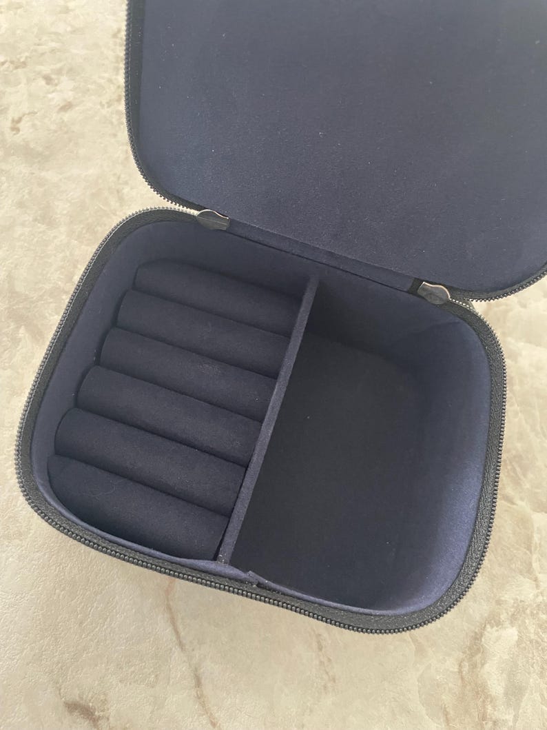 Op de afbeelding: Open marineblauwe sieradendoos met ritssluiting. De binnenkant heeft ringsleuven en een verdeeld compartiment. De doos is gevoerd met een zachte, donkerblauwe stof.