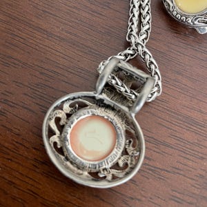 May include: Silver-toned necklace with a pendant featuring a round, peach-colored center. The pendant has an ornate, openwork design around the center. A matching silver-toned earring with a yellow center is also visible.