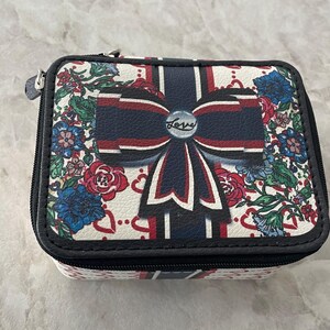 Op de afbeelding: Een rechthoekige sieradendoos met ritssluiting. De koffer heeft een witte achtergrond met een bloemenpatroon en een groot marineblauw strikdesign. Het woord "Love" staat op de strik. De koffer heeft een zwarte rand.