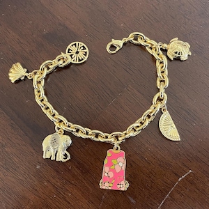 May include: Gold-toned charm bracelet featuring various charms, including a seashell, elephant, turtle, and a pink charm with a floral design. The bracelet has a lobster clasp closure and a chain link design.
