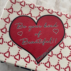 Op de afbeelding: Een rechthoekige etui met een rood hartontwerp en de tekst "Be your kind of Beautiful!!". De etui heeft een witte achtergrond met een patroon van rode harten. De tekst "BRIGHTON VTC" is ook zichtbaar.