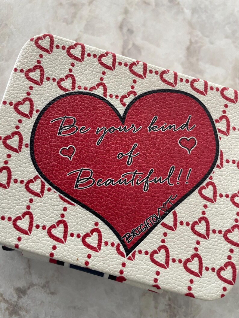 Op de afbeelding: Een rechthoekige etui met een rood hartontwerp en de tekst "Be your kind of Beautiful!!". De etui heeft een witte achtergrond met een patroon van rode harten. De tekst "BRIGHTON VTC" is ook zichtbaar.