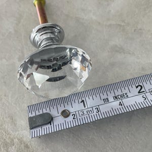 May include: A clear, faceted crystal cabinet knob with a chrome base and a threaded post. The knob is approximately 1.5 inches in diameter. A measuring tape is next to the knob.