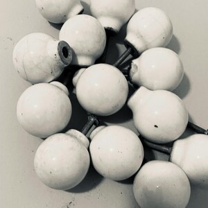 May include: A collection of white ceramic cabinet knobs with metal screws. The knobs are round with a glossy finish, some showing slight wear and age. The hardware is suitable for furniture restoration or DIY projects.