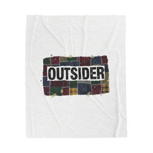 May include: White blanket with a patchwork design featuring the word "OUTSIDER" in black block letters. The patchwork is made of various fabric squares in shades of green, red, blue, and yellow, secured with safety pins and tape.