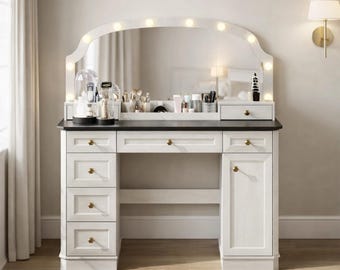 May include: A white vanity with a black countertop and a large, arched mirror with lights. The vanity has multiple drawers and a cabinet, with gold-colored knobs. Makeup brushes, skincare products, and decorative items are displayed on the vanity.