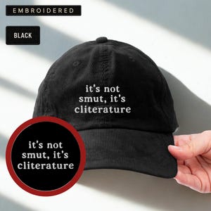May include: Black corduroy baseball cap with the embroidered text "it's not smut, it's cliterature." The cap has a curved brim and a top button. The word "BLACK" is printed on a small black rectangle.