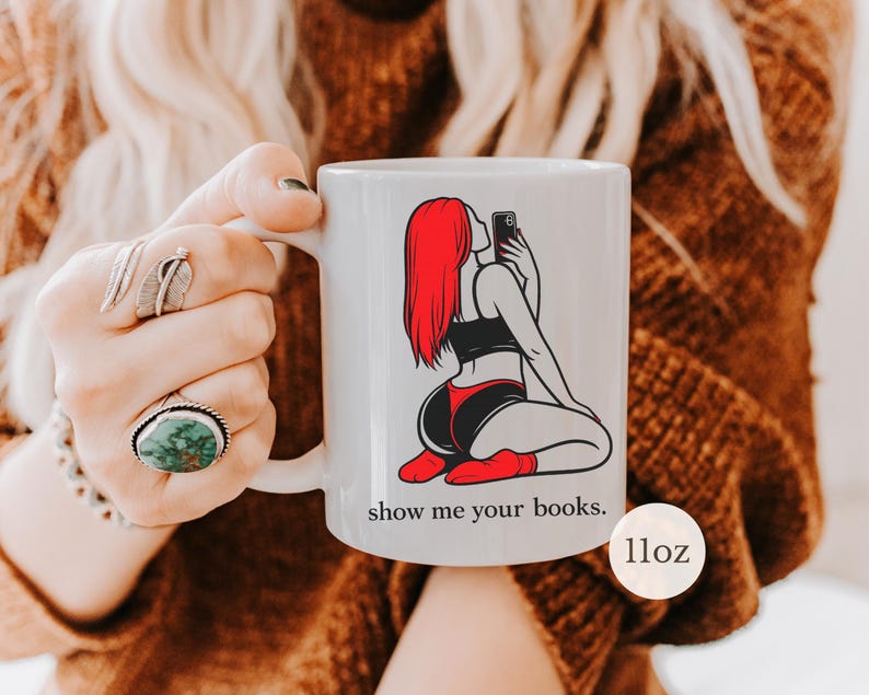 Pu&ograve; includere: Tazza in ceramica bianca con la grafica di una persona con i capelli rossi che si fa un selfie. La persona indossa un top nero, pantaloncini rossi e neri e calzini rossi. La tazza ha il testo "show me your books." ed &egrave; di 312 grammi.