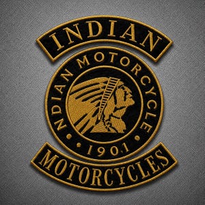 Op de afbeelding: Een zwart en goud geborduurde patch met het Indian Motorcycle logo. Het ontwerp bevat een centraal rond embleem met het profiel van een persoon met een hoofdtooi, omringd door de tekst Indian Motorcycle 1901, met gebogen banners.