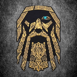 Può includere: Una toppa ricamata nera con un design color oro di ispirazione norrena che raffigura un volto barbuto con intricati motivi a intreccio. Il design include un dettaglio di un occhio blu brillante e elementi di capelli intrecciati simmetrici in filo d'oro.