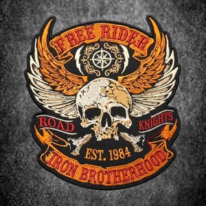 Może przedstawiać: Haftowana naszywka z centralnie umieszczoną czaszką i dużymi pomarańczowo-białymi skrzydłami. Tekst głosi FREE RIDER, ROAD KNIGHTS, EST. 1984 oraz IRON BROTHERHOOD. Wzór zawiera gwiazdę kompasu i wstęgi z napisami na czarnym tle.