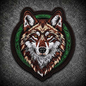 May include: An embroidered patch featuring a detailed wolf head with brown, white, and black fur. The wolf is centered within a circular frame that has a dark brown border and an inner ring of green, intricate, knot-like geometric patterns.