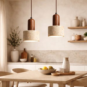 Puede incluir: Dos lámparas colgantes con una pantalla cilíndrica beige texturizada y una parte superior de madera oscura. Las luces cuelgan de cables marrones. La imagen es de un comedor con una mesa de madera, un jarrón y un cuenco de fruta.