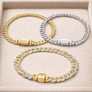 Pode incluir: Três pulseiras de corrente com fechos retangulares gravados com a palavra Pandora. Uma pulseira é dourada, uma é prateada e a terceira é um design bicolor com elos alternados de ouro e prata com pedras transparentes incrustadas.
