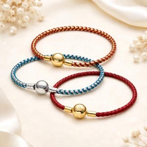 Può includere: Tre bracciali intrecciati con chiusure rotonde. Un bracciale ha una fascia intrecciata rossa con una chiusura dorata. Un altro ha una fascia intrecciata blu con una chiusura argentata con il marchio Pandora. Il terzo ha una fascia rossa con una chiusura dorata.