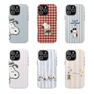 May include: Six smartphone cases featuring Snoopy illustrations. Designs include blue stripes, red gingham, blue stripes with text 'Don't overthink it', pink stripes, blue watercolor stripes with multiple Snoopy figures, and pink stripes with stars and text.