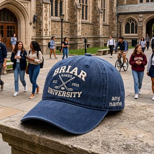 May include: A navy blue baseball cap featuring embroidered text that reads Briar University, Hawks, Est. 2015, and a crossed hockey stick graphic. The side of the cap includes the embroidered text any name in white lettering on a structured fabric.