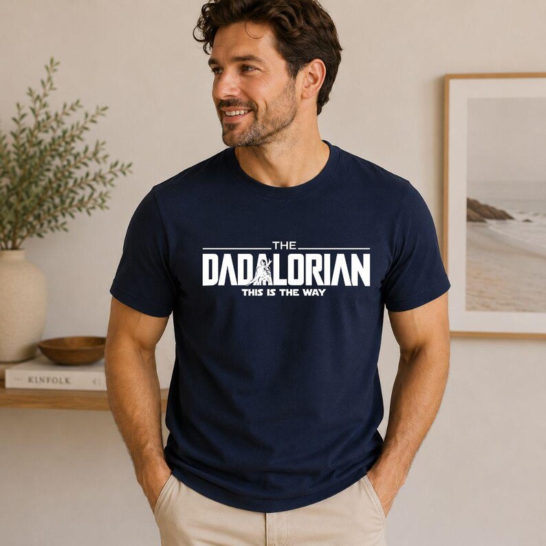 May include: A navy blue short-sleeved t-shirt featuring white screen-printed text that reads THE DADALORIAN and THIS IS THE WAY, with a small graphic of a figure integrated into the letter A in the word DADALORIAN on the center of the chest.