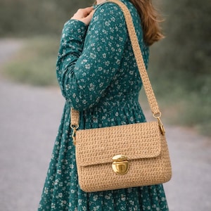 Peut inclure: Un sac à bandoulière rectangulaire en crochet beige avec un motif tissé texturé, une fermeture à poussoir en métal doré et une bandoulière en crochet assortie fixée par des anneaux en métal doré sur les côtés du sac.