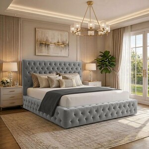 May include: A grey button-tufted bed with a high headboard and base. The bed is dressed with cushions and a dark grey throw. The room includes a chandelier, bedside tables with lamps, and a large painting on the wall.
