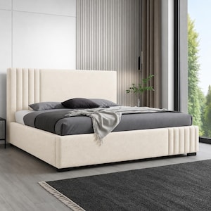 May include: A cream-coloured upholstered bed with a tall, vertically-lined headboard. The bed frame has a matching cream colour and a low profile. The bed is made up with grey bedding and a grey throw blanket. A black rug is in the foreground.