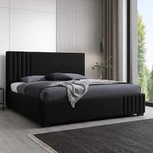 May include: A contemporary black upholstered bed with a tall, vertically-lined headboard. The bed has a low profile frame and is dressed with grey bedding and pillows. A grey throw blanket is draped across the foot. The bed sits on a light grey floor.