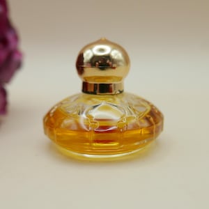 May include: A small, round, clear glass perfume bottle filled with amber-coloured liquid. The bottle features a faceted, textured surface and is topped with a smooth, shiny, gold-coloured spherical cap that sits securely on the neck of the bottle.