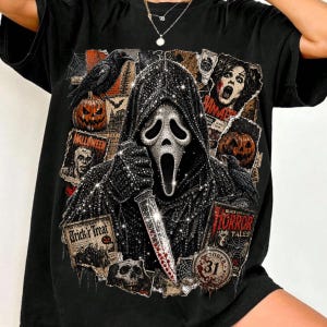 May include: A black t-shirt featuring a graphic print of a hooded figure with a white mask holding a knife. The design includes various Halloween-themed elements such as a jack-o'-lantern, a raven, a skull, and text reading Trick r Treat.