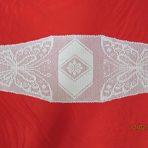 May include: White crocheted table runner with a diamond pattern in the center and a floral design on each end.