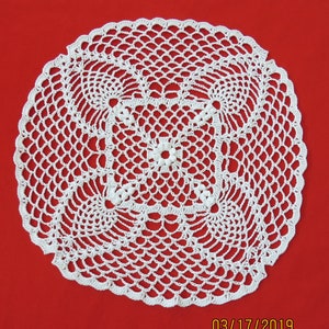 May include: White crocheted doily with a delicate floral pattern, on a red background. 03/17/2019 is written in the bottom right corner.
