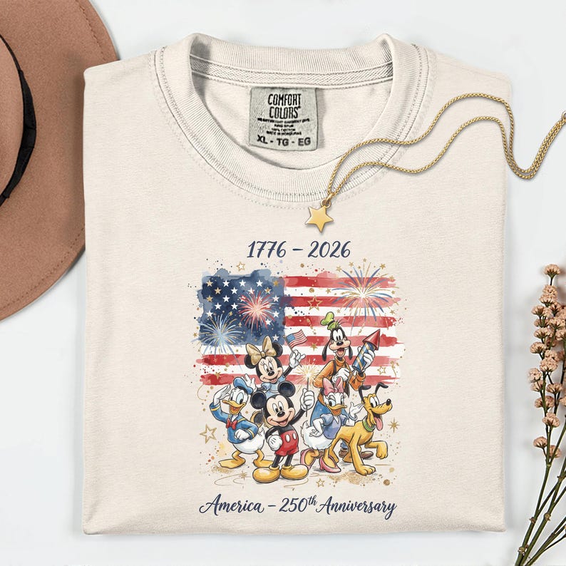A ivory Comfort Colors t-shirt featuring festive cartoon friends in front of a US flag graphic celebrating America's 250th Anniversary.