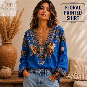 Op de afbeelding: Een felblauw shirt met lange mouwen, een diepe V-hals en ingewikkeld veelkleurig bloemenborduursel op de borst en mouwen. Het shirt heeft decoratieve patronen langs de halslijn en manchetten en wordt gecombineerd met een lichtblauwe spijkerbroek.