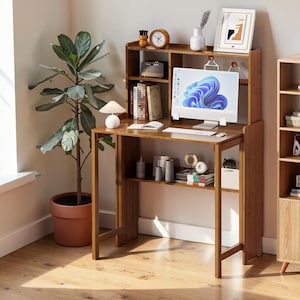 May include: A wooden desk with a hutch, featuring a computer monitor, books, and decorative items. The desk has a warm, natural wood finish and includes a lower shelf for storage. A potted plant is visible in the background.