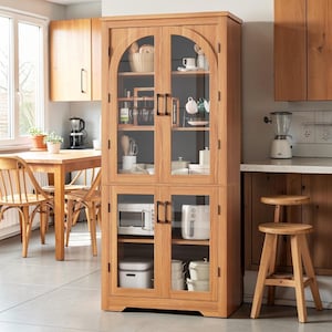 May include: A light brown wooden kitchen cabinet with glass doors. The cabinet has two sections, with shelves displaying kitchen items like dishes, cups, and a microwave. The cabinet is in a kitchen with a wooden table and chairs.