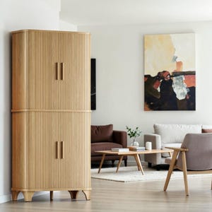 May include: A tall, light-toned wooden cabinet featuring a vertical slatted design on its exterior. The cabinet is divided into two sections, each with a pair of doors equipped with matching vertical wooden handles, supported by four short legs.
