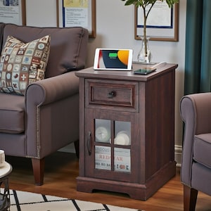 May include: A dark brown wooden end table featuring a single top drawer with a square knob and a lower cabinet with a glass-paneled door. The cabinet door has a black handle and reveals two stacked books with visible text including REDSTAR.