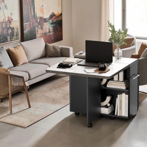 May include: A dark gray mobile desk with a light gray rectangular top, featuring open shelving on one side filled with books and decorative items. A black laptop, a dark mug, and a notebook are placed on the desk surface, which sits on wheels.