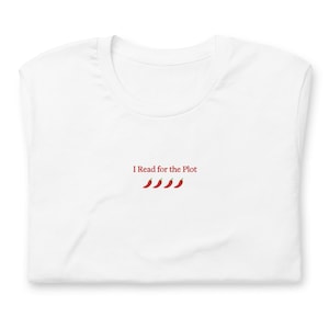 May include: A white t-shirt featuring the red text "I Read for the Plot" centered on the chest. Below the text are four small, red chili pepper icons arranged in a horizontal row. The shirt has a classic crew neckline and short sleeves.