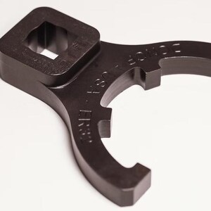 May include: A black wrench with a square socket and curved arms. The wrench has the text "ER" and "36" on it. The tool is designed for specific applications and is made of durable material.