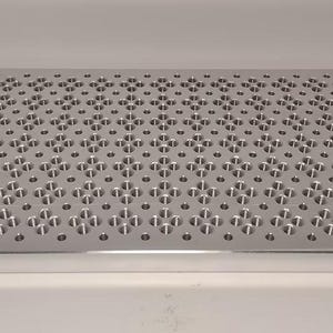 May include: A rectangular, silver-colored metal plate with a grid of evenly spaced, small circular holes. The plate has a matte finish and appears to be made of aluminum or a similar alloy. The holes are arranged in a repeating pattern.