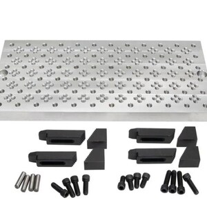 May include: A silver-colored metal work surface with numerous holes and a set of black clamps, screws, and pins. The surface is rectangular and designed for precision work. The components are arranged below the main plate.
