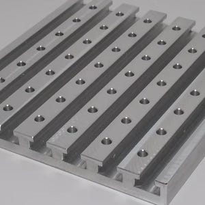May include: A rectangular, silver-colored metal plate with evenly spaced, raised bars. Each bar has multiple drilled holes. The plate has a machined appearance, suggesting precision engineering or manufacturing.