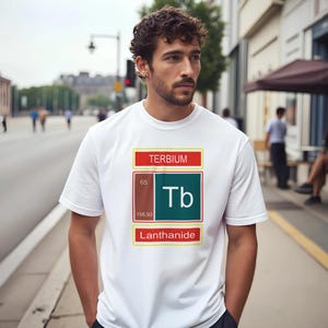 Peut inclure: Un t-shirt blanc à manches courtes arborant un graphique de l'élément chimique Terbium. Le motif comprend le numéro atomique 65, le symbole Tb, le poids atomique 158,93, ainsi que le texte Terbium et Lanthanide dans un cadre rectangulaire.