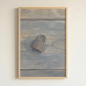 May include: Framed artwork depicting a weathered padlock on a painted wooden surface. The wood has a blue-grey hue with visible grain and texture. The padlock is metallic and appears aged, adding to the rustic aesthetic. The artwork is encased in a light-coloured wooden frame.