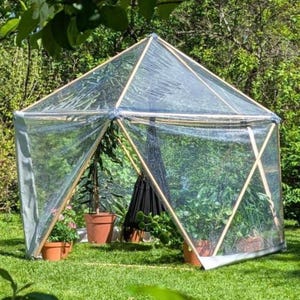 Puede incluir: Un cenador de jardín hexagonal con estructura de madera y paneles de plástico transparente. Dentro de la estructura hay plantas en macetas y una silla colgante negra. El cenador está situado sobre un césped verde rodeado de árboles.